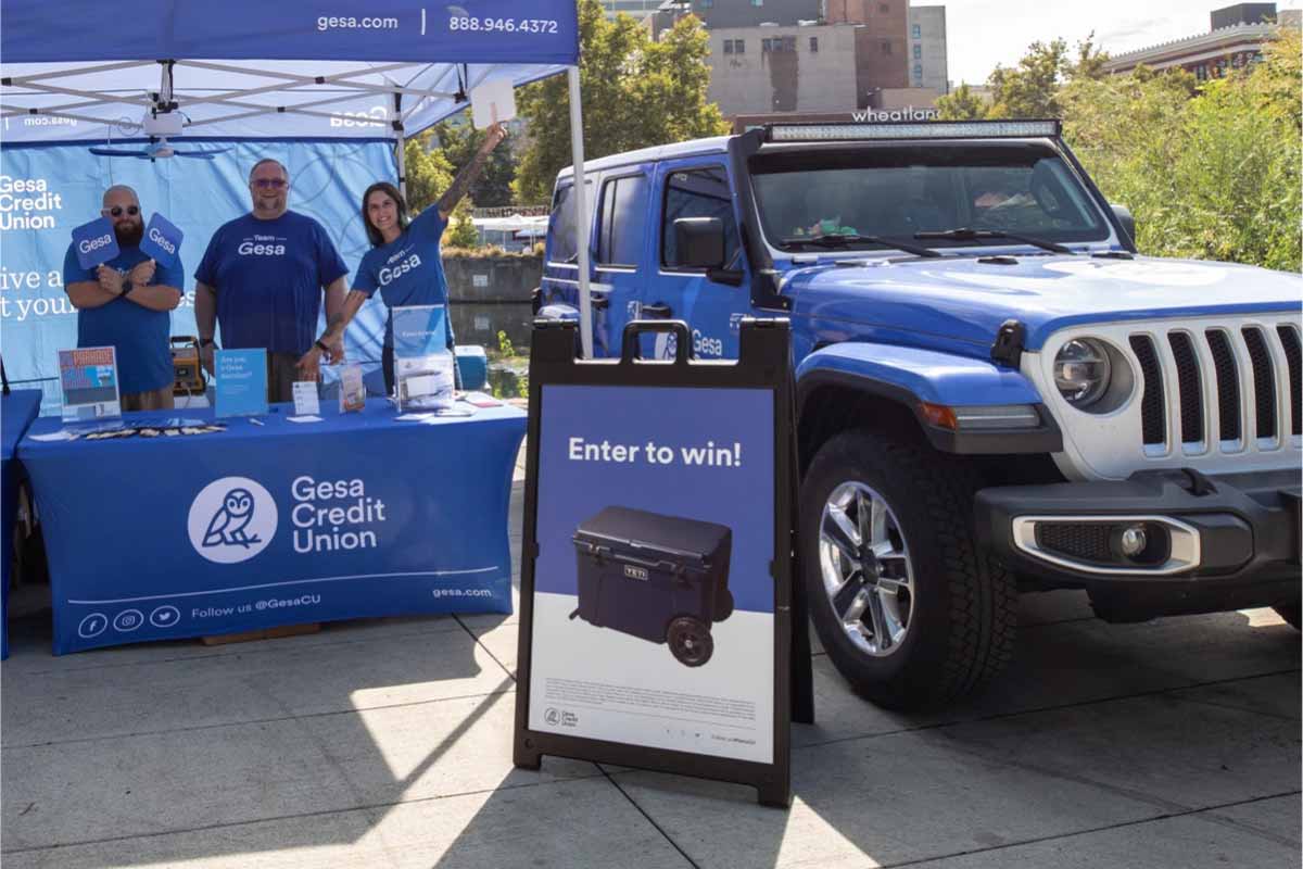 Gesa Credit Union booth with staff, promotional materials, and a Jeep, featuring a sign promoting a giveaway for a cooler.